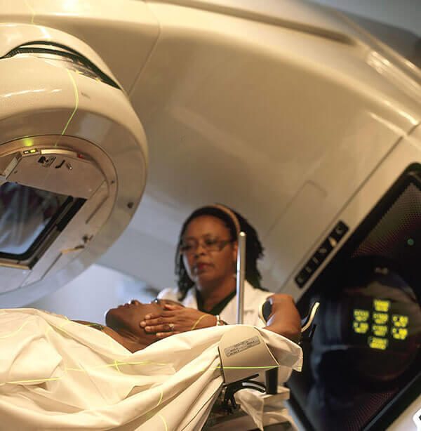 Installation d’une patiente sur une table de radiothérapie par une professionnelle. Photographie documentaire du National Cancer Institute.